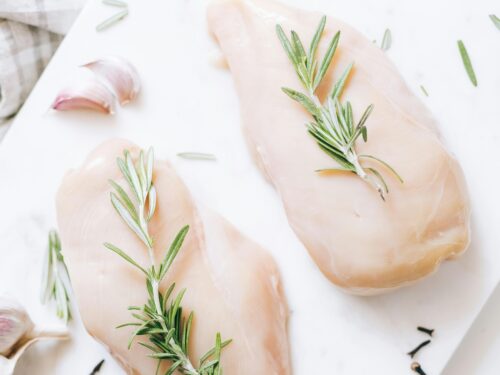 High-angle view of raw chicken breasts on marble with rosemary and garlic, ideal for healthy recipe inspiration.