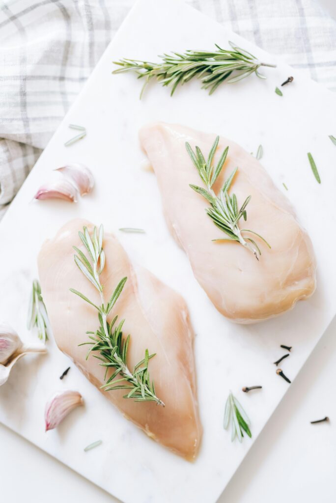 High-angle view of raw chicken breasts on marble with rosemary and garlic, ideal for healthy recipe inspiration.