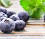 Close-up of fresh blueberries on a bamboo surface with green leaves.