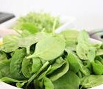 A close-up of fresh spinach leaves in a white bowl, ideal for healthy salads.