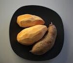 Three sweet potatoes on a black plate, showcasing fresh and rustic appeal.