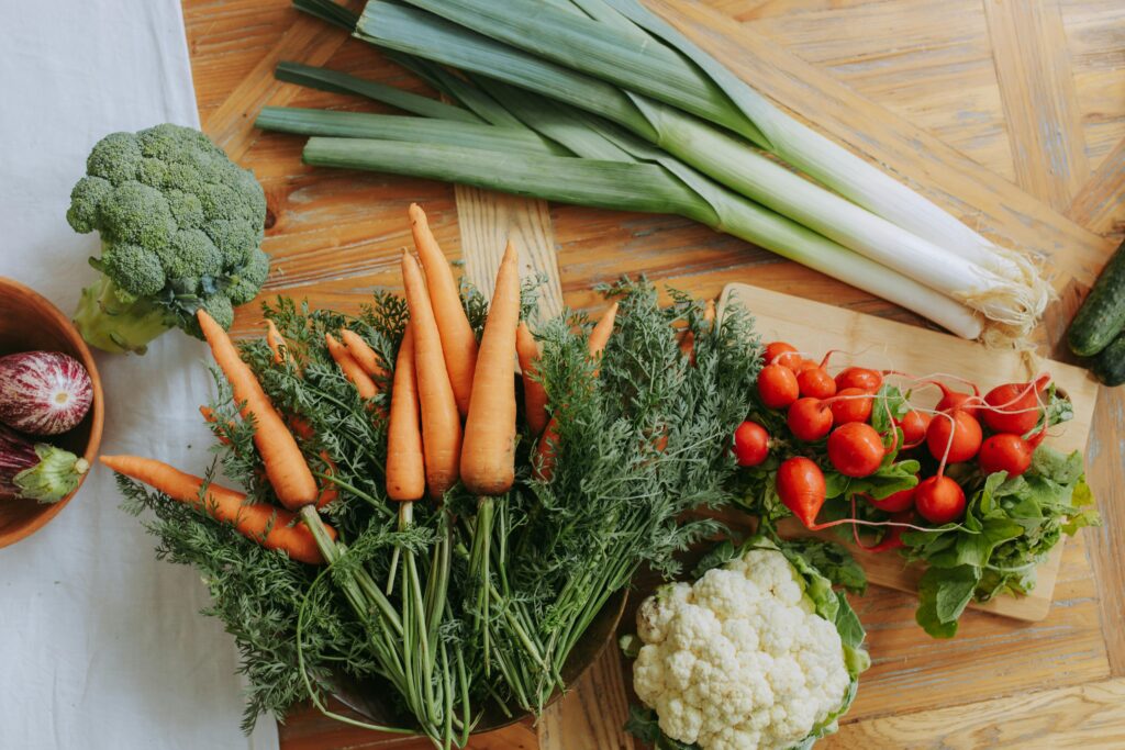 A colorful assortment of fresh vegetables including carrots, leeks, and radishes displayed on a wooden table.