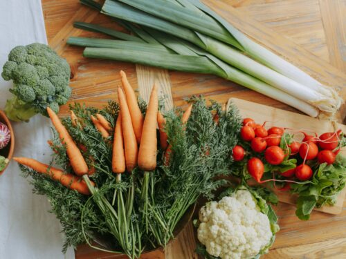 A colorful assortment of fresh vegetables including carrots, leeks, and radishes displayed on a wooden table.