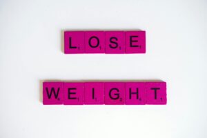 Creative image of the phrase 'Lose Weight' spelled with Scrabble tiles on a white background.